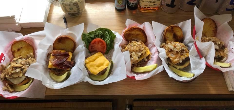 Several burgers with various toppings on a wooden table