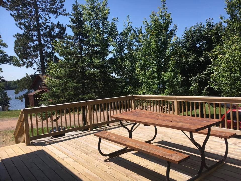 A wooden deck with a railing overlooking a lake surrounded by trees.