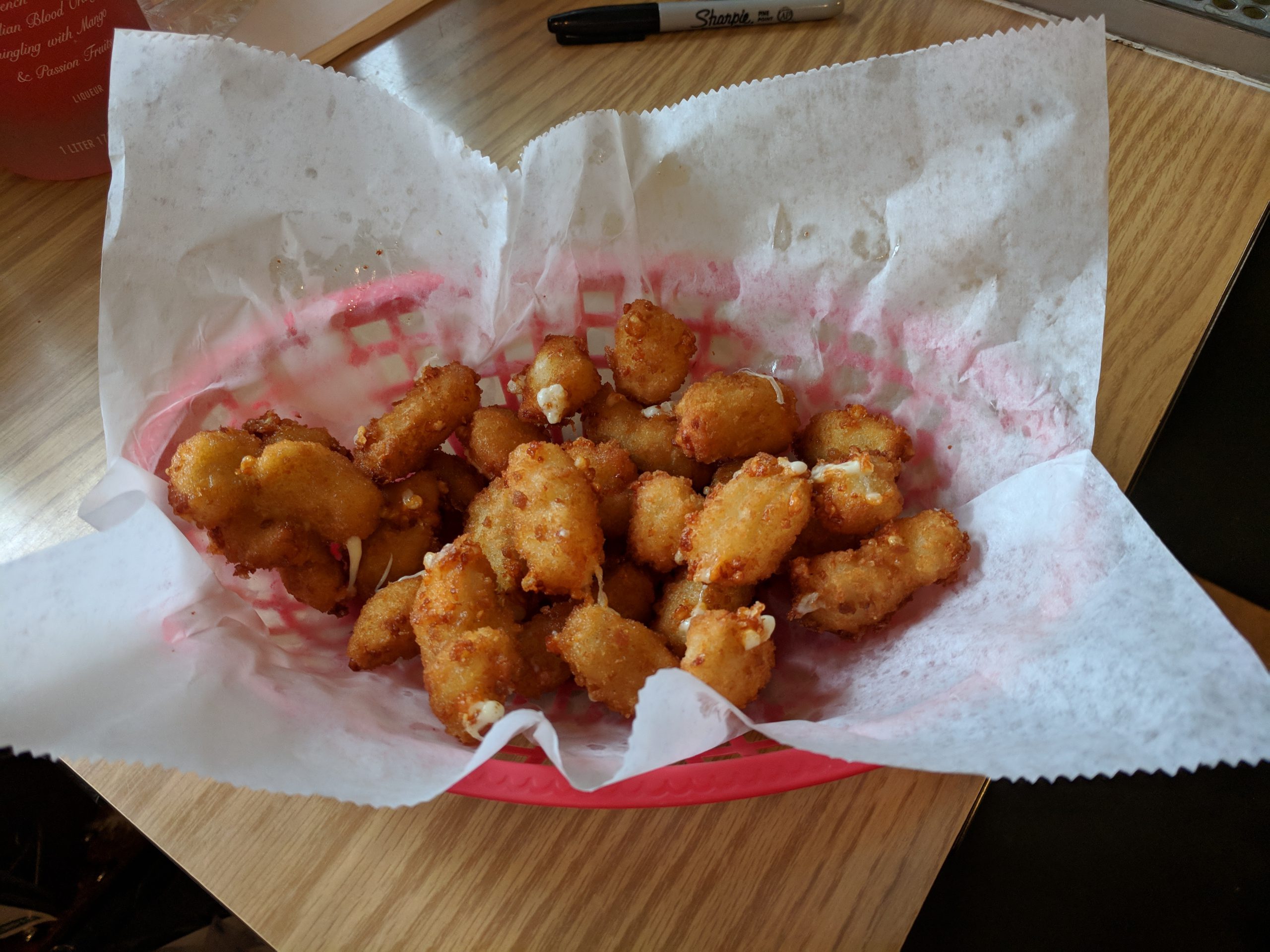 A red basket lined with paper contains fried food on a wooden table.