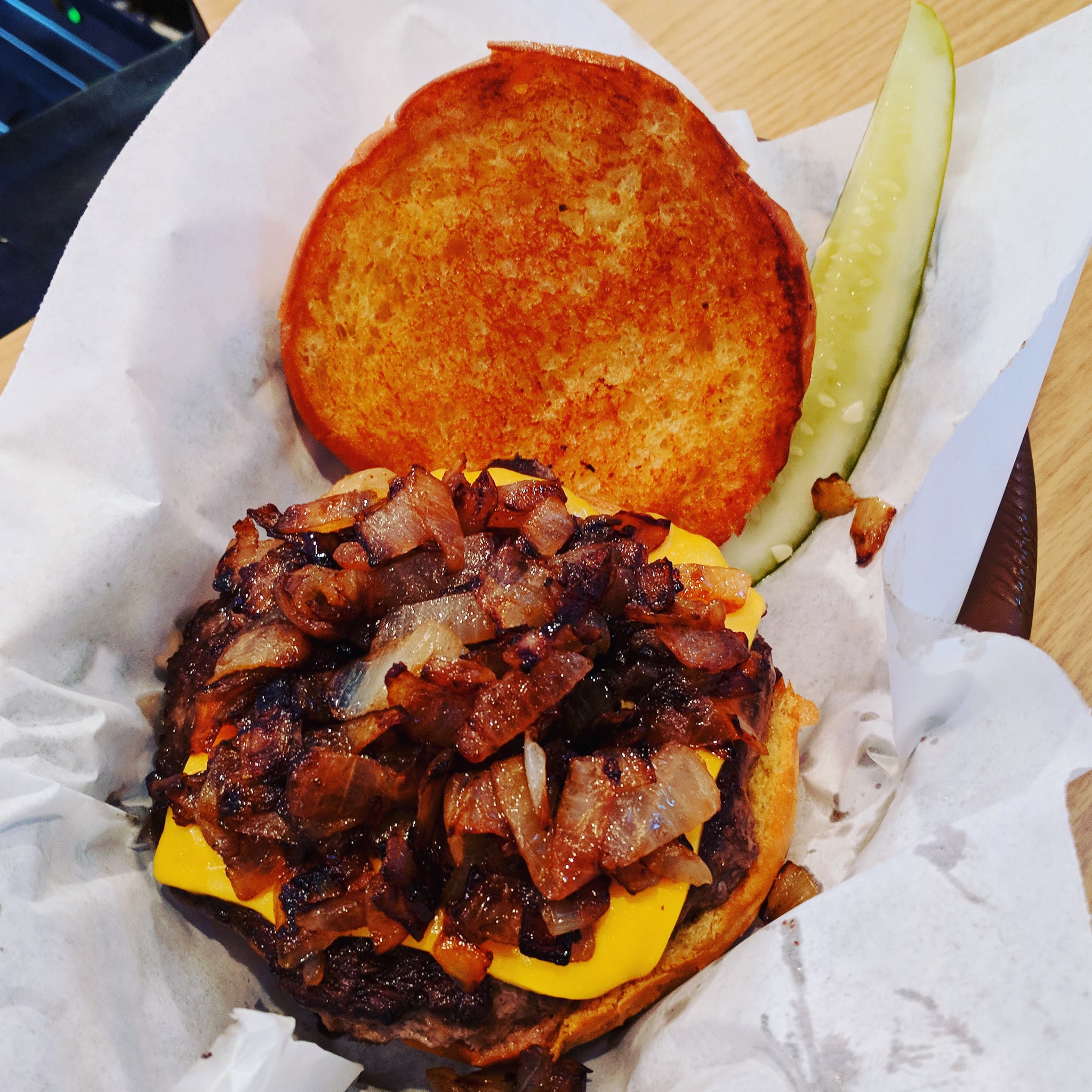 a burger with bacon and cheese and a slice of cucumber