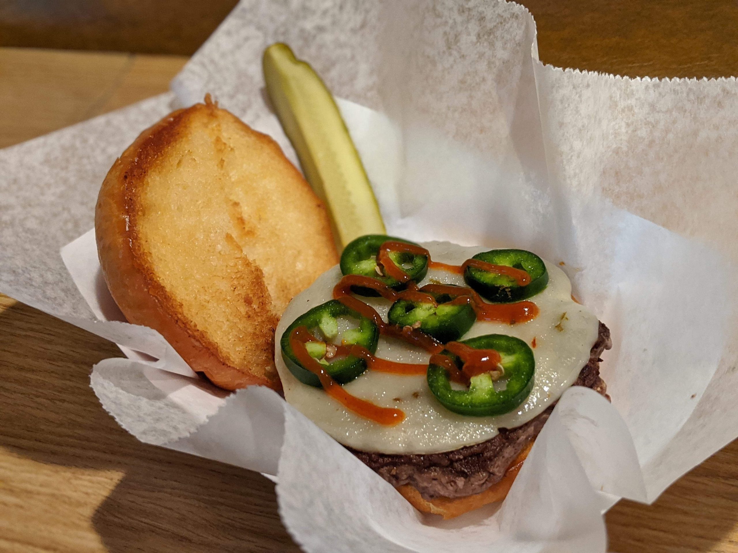 a burger with jalapenos and cheese on a wooden table